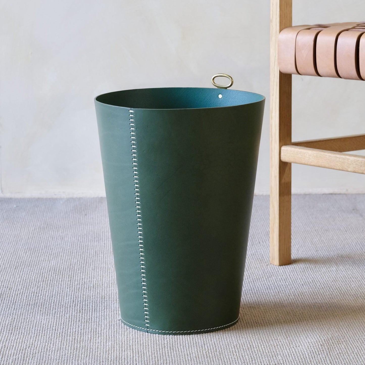 Dark green leather eyelet wastepaper bin with white stitching and gold tone handle for stylish trash disposal