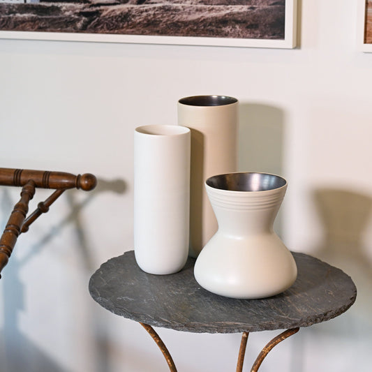 Three minimalist ceramic canna wide small vases in white and beige with sleek shapes and metallic silver interiors