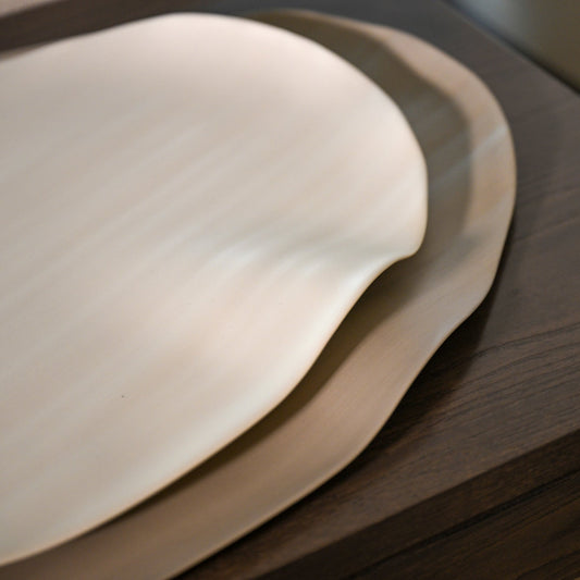 Cream-colored smooth ceramic plate with gently curved edge from leaf large linen collection
