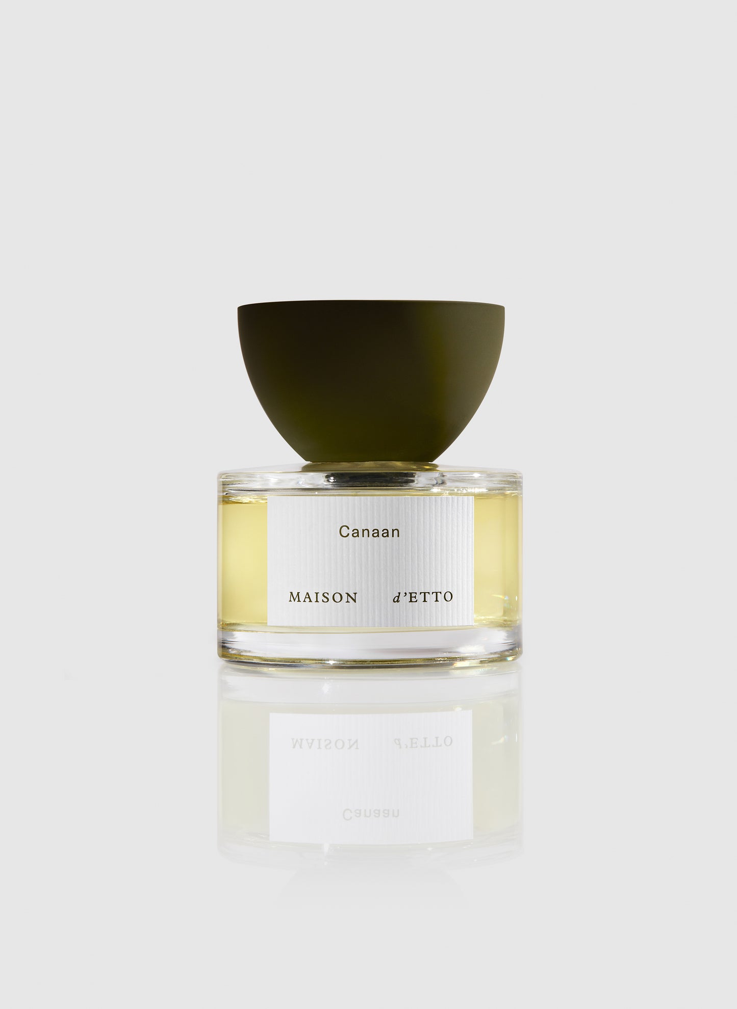 A sleek transparent glass perfume bottle with a matte olive-green cap and minimalist white canaan label by Maison dEtto