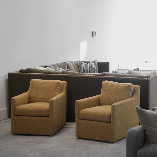 Two mustard yellow plush custom order carmel swivel chairs with modern boxy design in front of dark gray sectional sofa