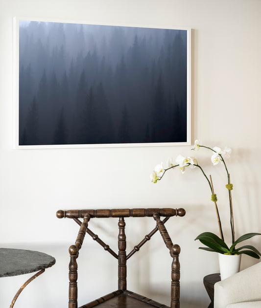 A framed photographic print titled ghost of day break featuring a misty forest in deep blues and grays in a white frame