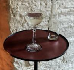 A clear martini glass on a dark red hand forged iron side table with optional leather insert