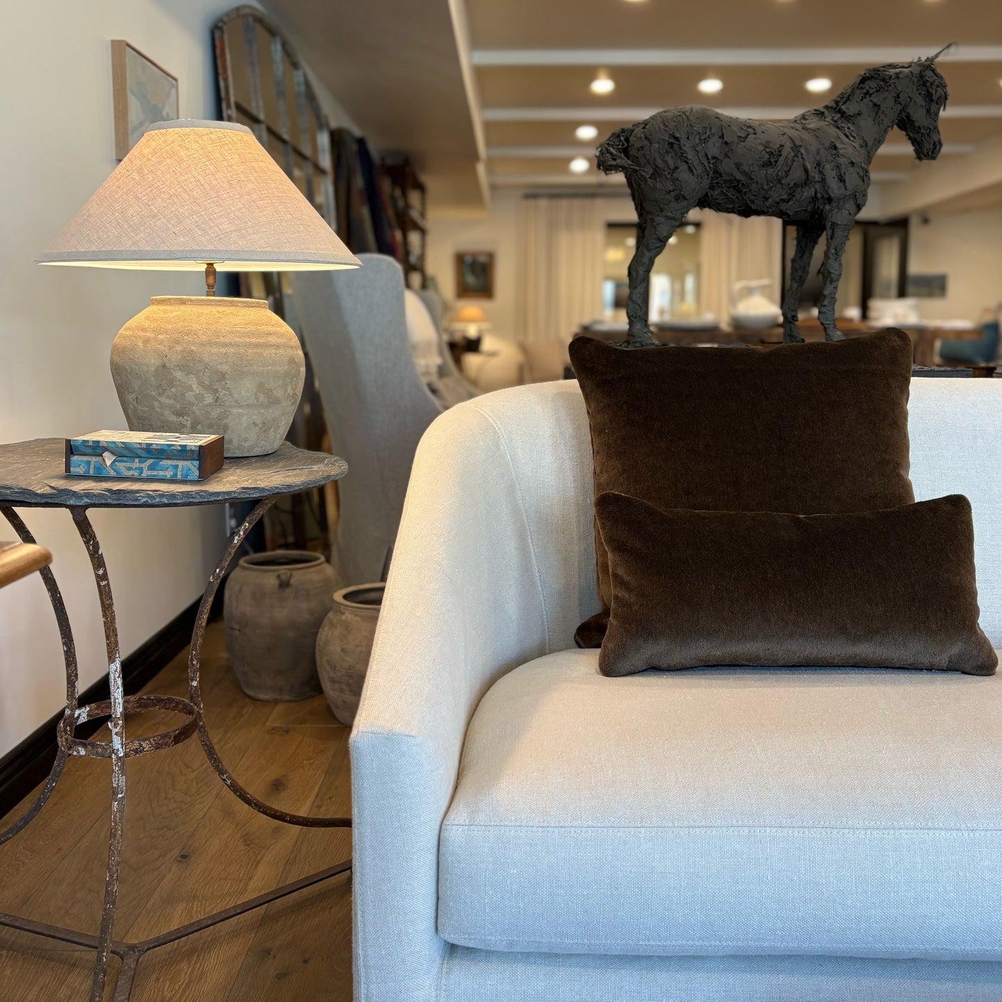 A dark textured metal unicorn sculpture standing atop a cushioned mohair pillow 20x10 on a sofa