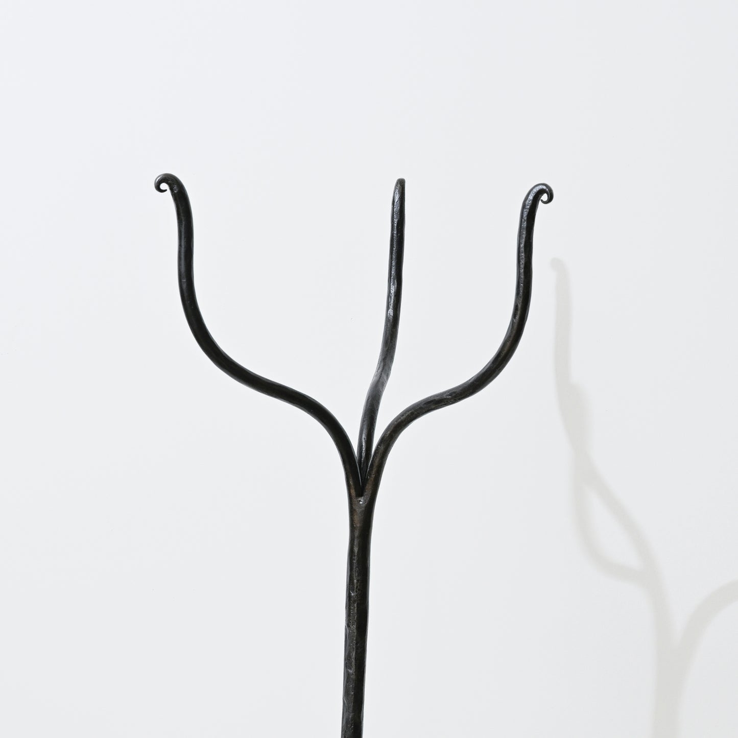 Black wrought iron coat hanger with three curved arms on hand forged iron side table