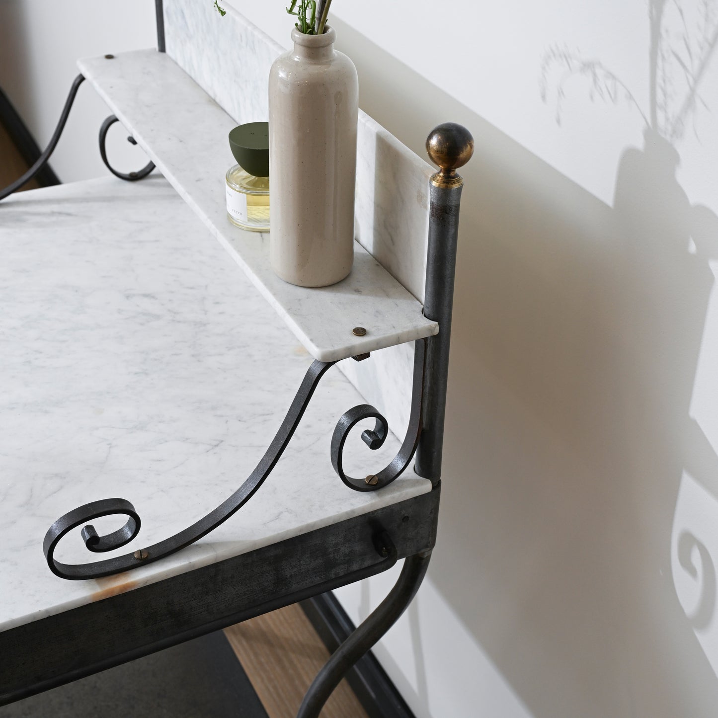 Elegant early 20th century marble vanity with a marble top, black wrought iron legs, ornate scrollwork, and brass finial accents