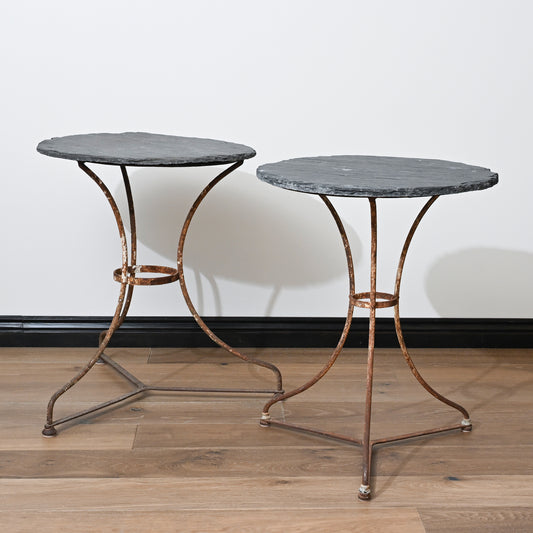 Two antique French slate bistro tables with dark gray irregular slate tops and warm bronze wrought iron legs