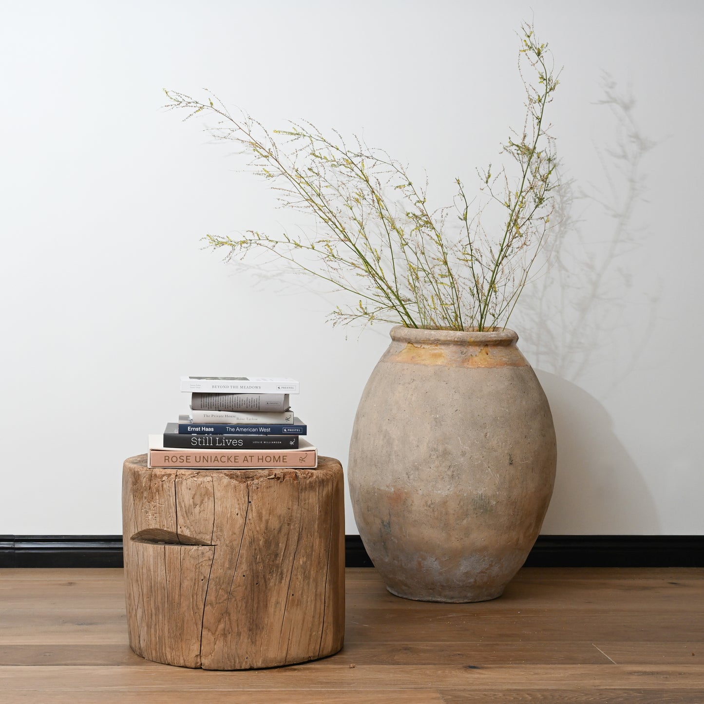 A rustic earth-toned ceramic vase with rounded body and flared rim holding greenery on a late 19th century primitive japanese mortar table