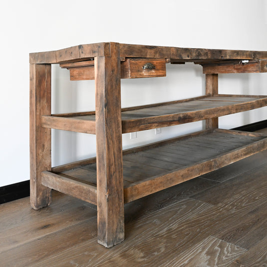 Rustic wooden antique French workbench console table with three shelves and single drawer featuring ornate metal pull