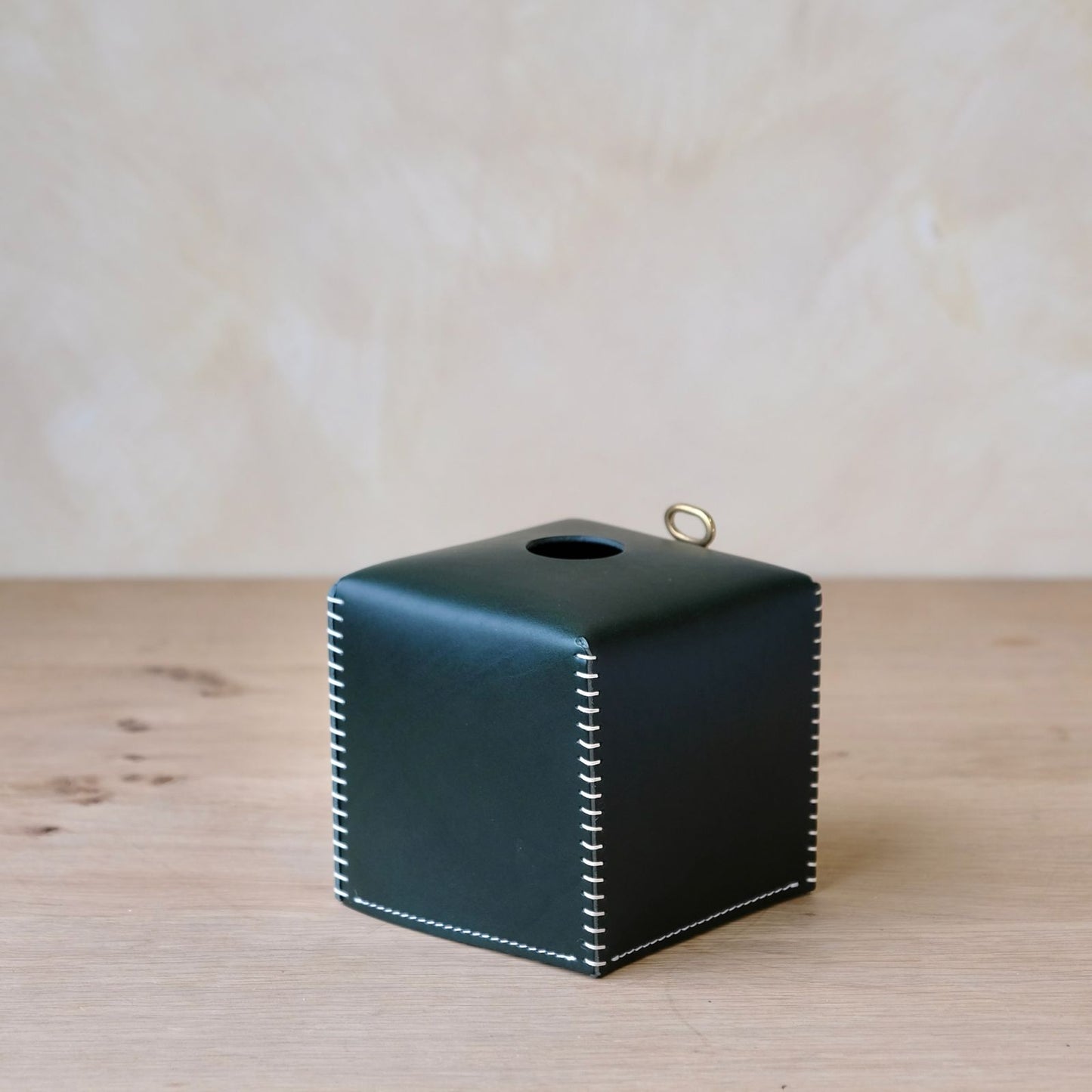Leather tissue box cover in black leather with white stitching and a gold-tone ring on top for stylish tissue storage
