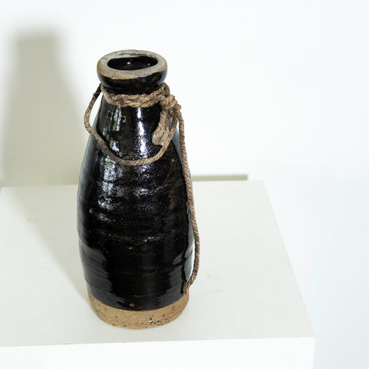 Black ceramic bottle with rope handle on a white surface