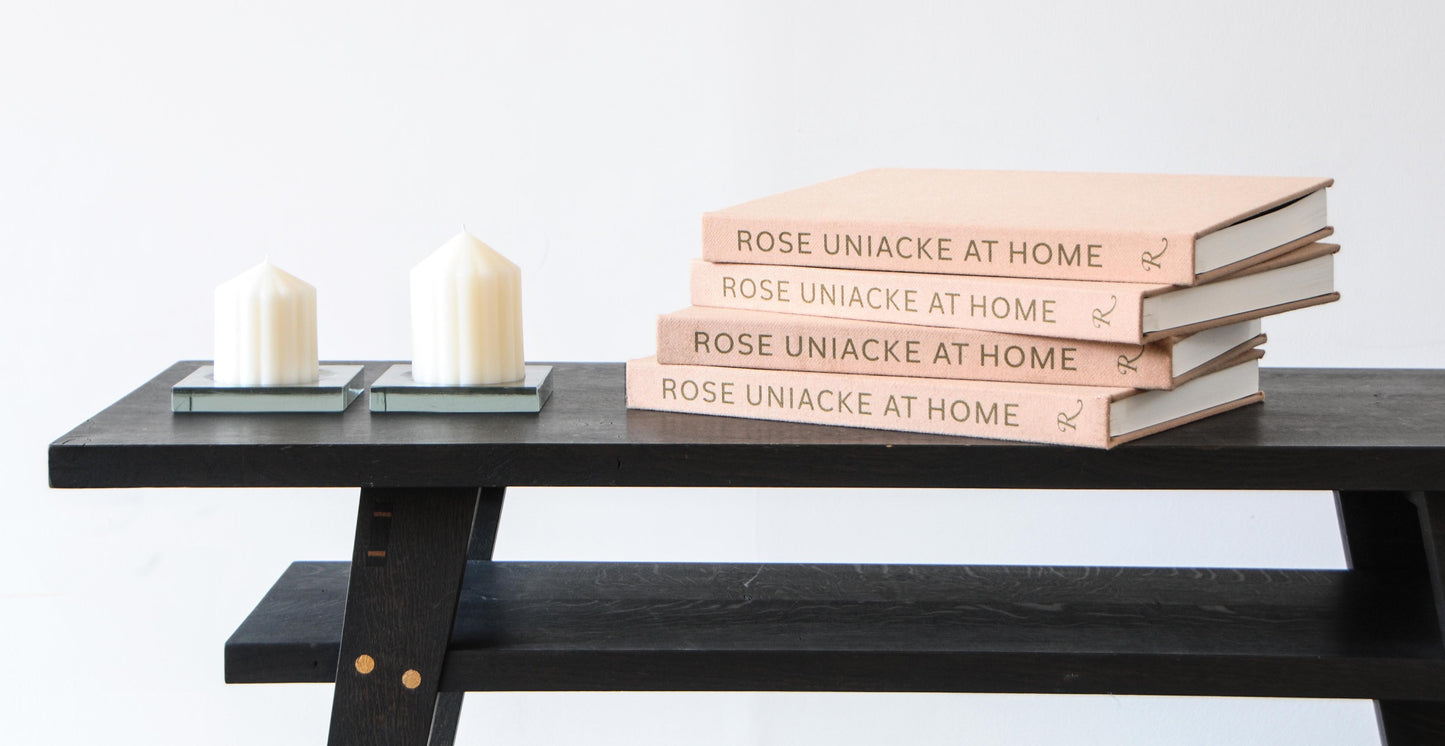 Stack of four pale pink hardcover books titled rose uniacke at home with minimalist black lettering and monogrammed r spine