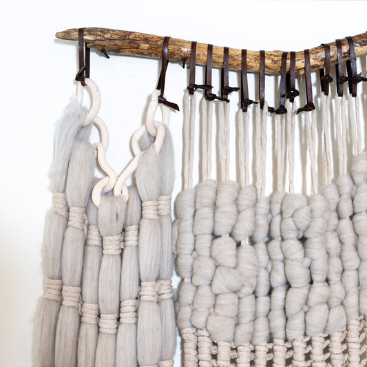 Textile art piece with braided yarn on a wooden frame against a white background