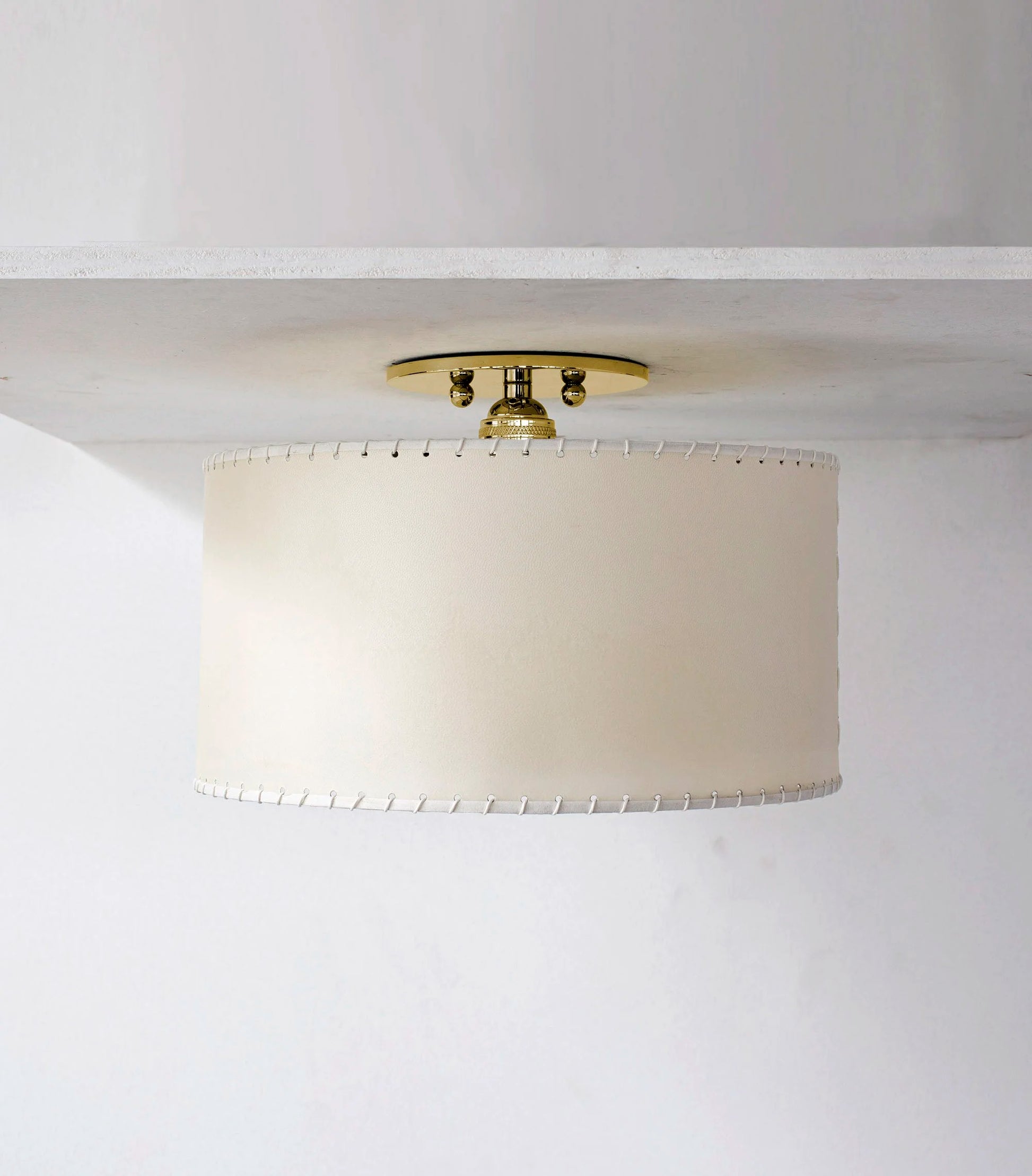 Cream-colored parchment flushmount with cylindrical lampshade and white stitching on brass ceiling fixture