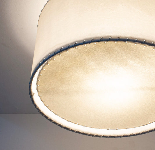 Cream-colored parchment flushmount with a cylindrical textured lampshade and dark blue stitching along the rim