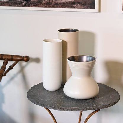 Three minimalist ceramic vases in crème with sleek cylindrical and hourglass shapes and metallic interiors