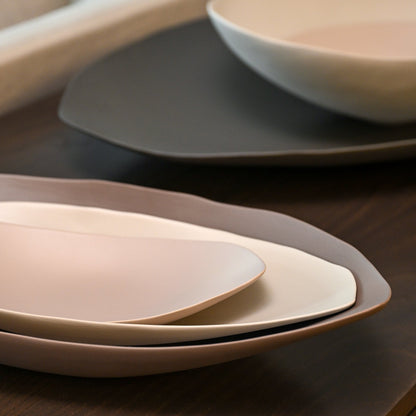 Stacked minimalist barchetta strette large ceramic plates in dark turtledove soft beige and muted gray tones with curved edges