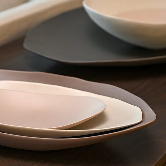 Stacked minimalist barchetta strette large ceramic plates in dark turtledove soft beige and muted gray tones with curved edges