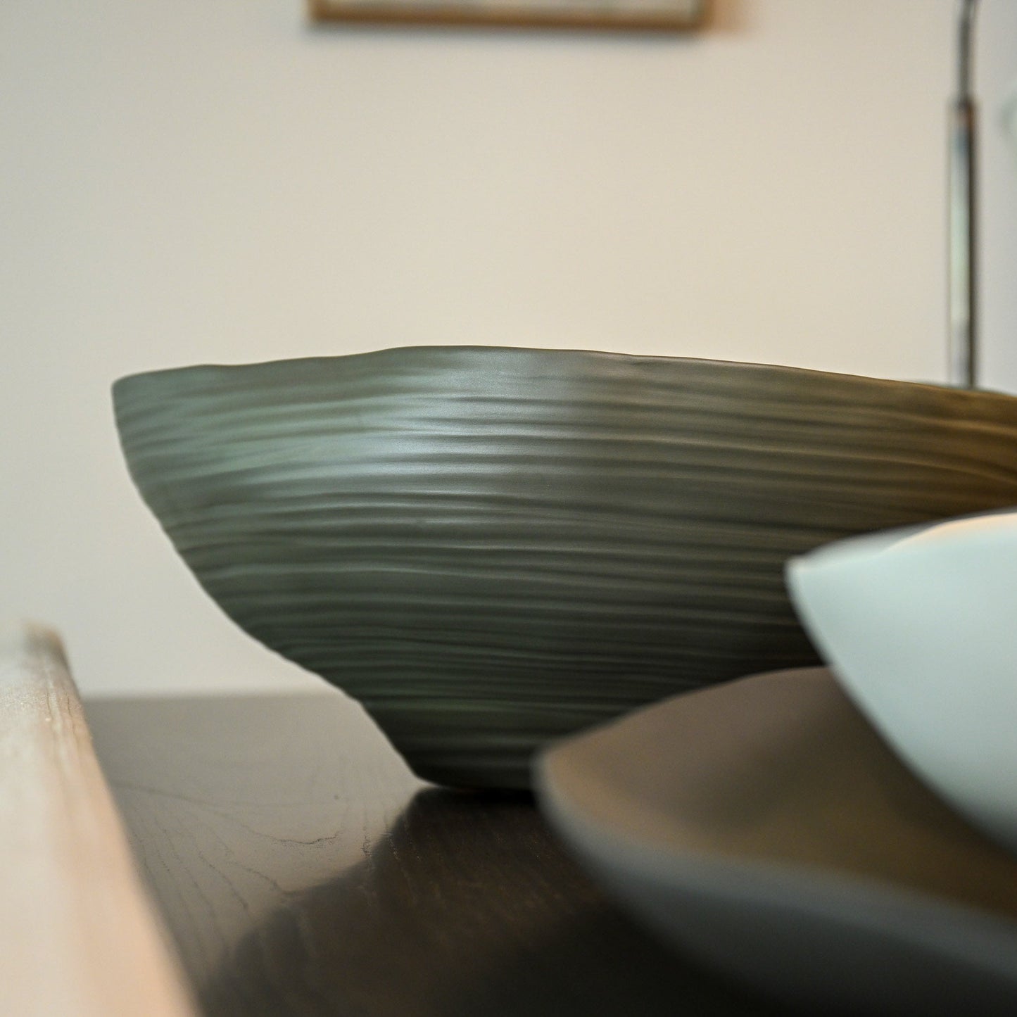 A sleek dark green ceramic bowl with subtle horizontal ridges and a smooth glossy finish called Fonte Medium Moss