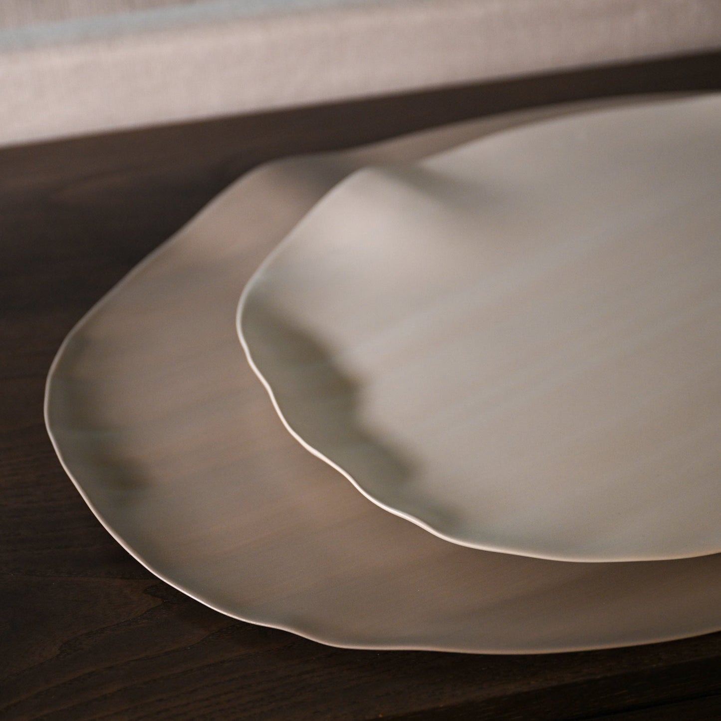 Two overlapping leaf xlarge ceramic plates with matte finish and wavy edges in light brown off-white hue