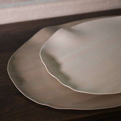 Two overlapping leaf xlarge ceramic plates with matte finish and wavy edges in light brown off-white hue