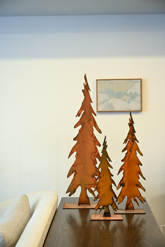 Three rust-colored patinated metal tree sculptures with weathered textured finish on wooden bases
