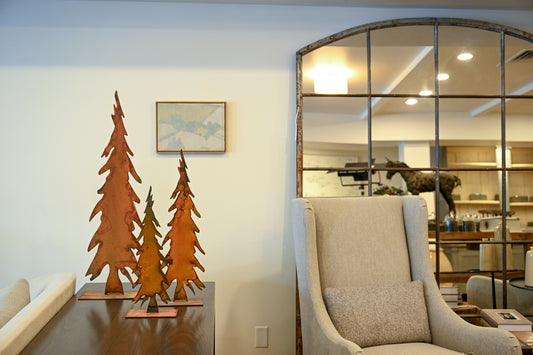 Three rust-colored patinated metal tree sculptures displayed on a dark wooden table for home decor