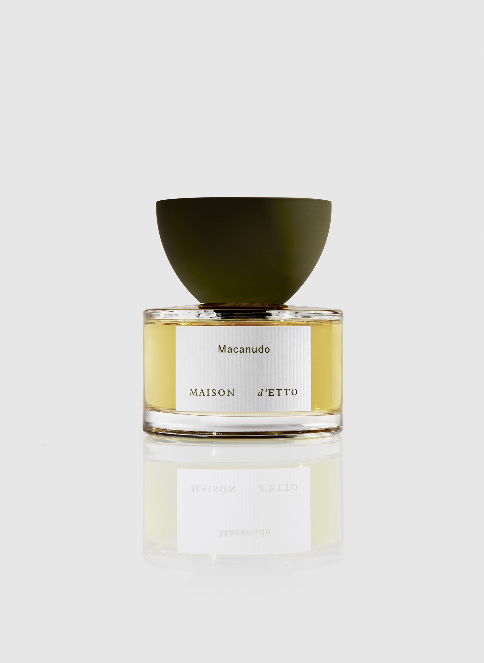 A sleek transparent glass perfume bottle with a matte olive green bowl cap and silver macañudo label by Maison dEtto