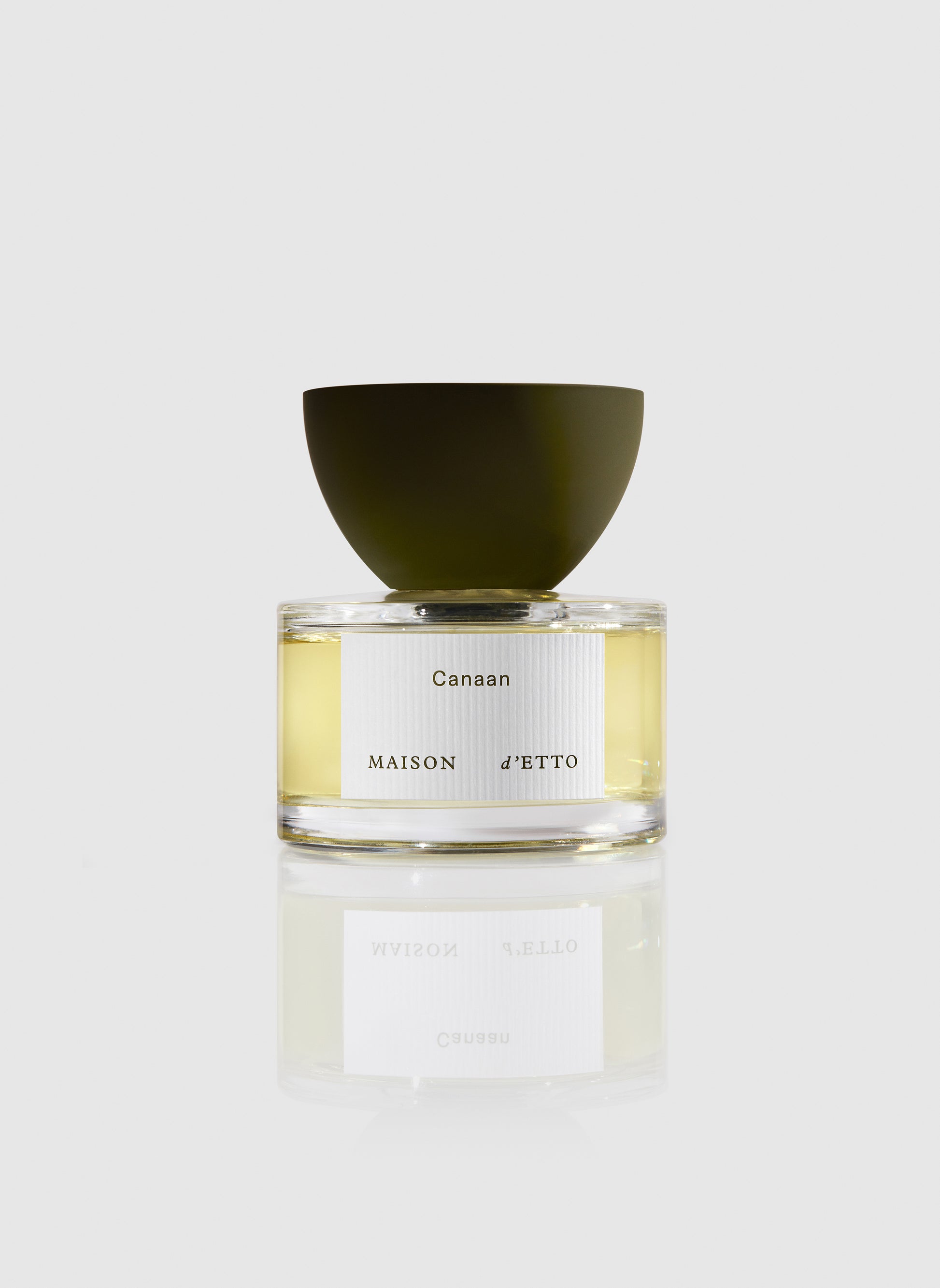 A sleek transparent glass perfume bottle with a matte olive-green cap and minimalist white canaan label by Maison dEtto