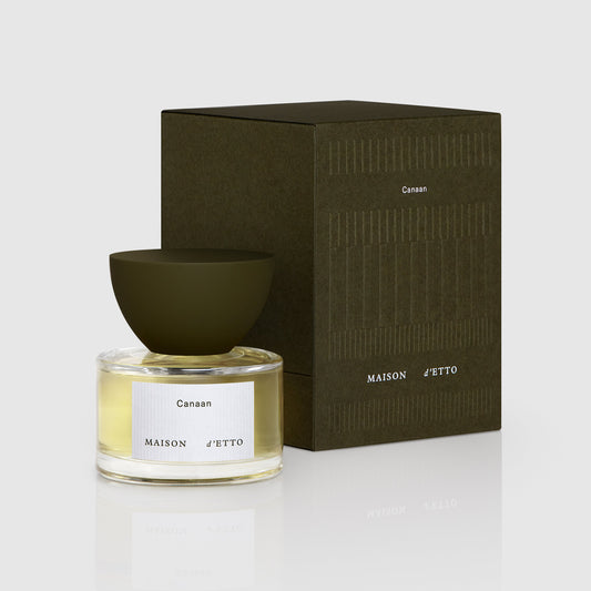 A sleek transparent glass bottle with a matte olive green bowl cap and a white label reading canaan by maison d etto