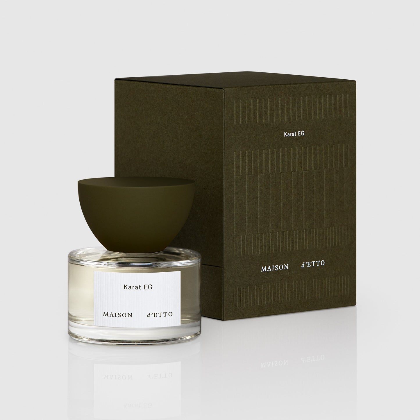 A minimalist glass perfume bottle with a matte olive green bowl cap and clear liquid labeled karat eg by Maison dEtto