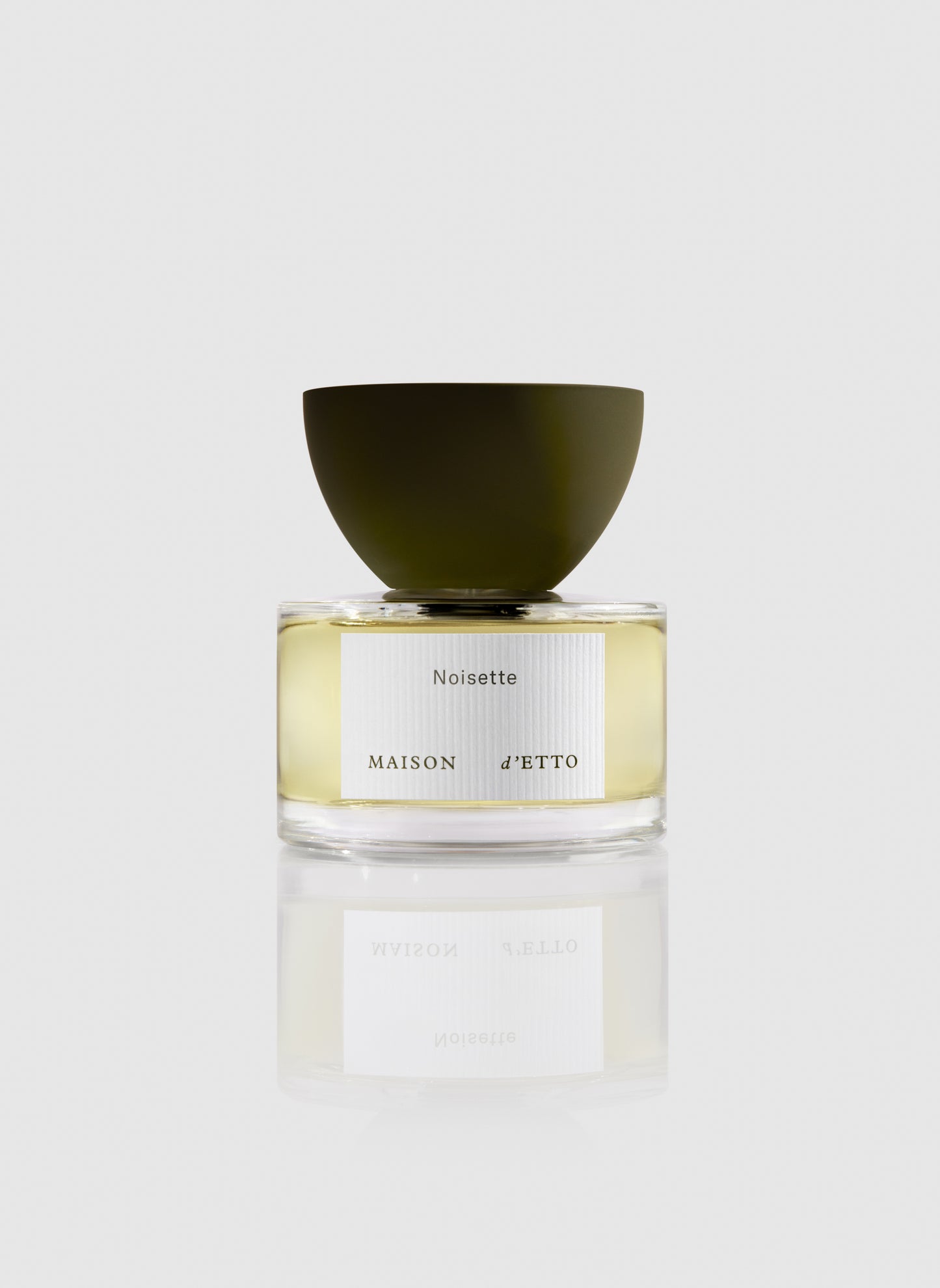 A sleek transparent glass perfume bottle with a matte olive green cap and minimalist noisette label by Maison d Etto