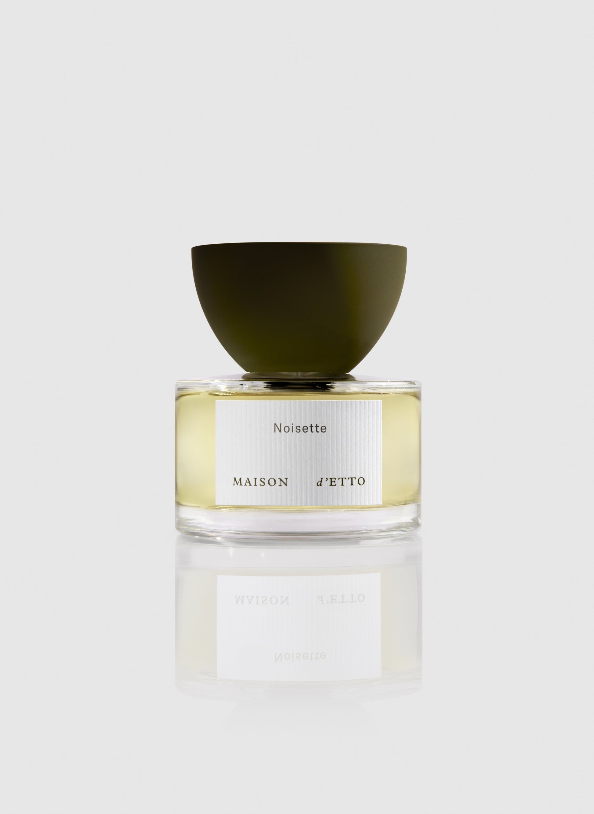 A sleek transparent glass perfume bottle with a matte olive green cap and minimalist noisette label by Maison d Etto
