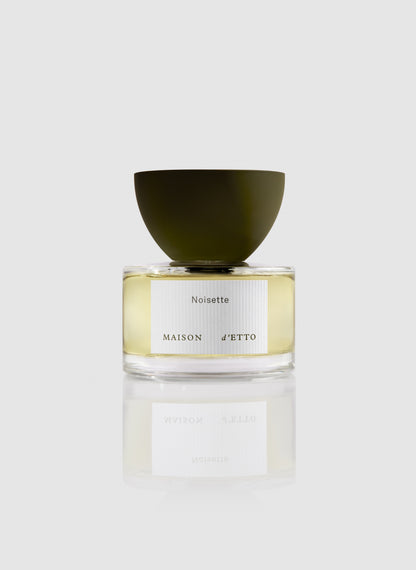 A sleek transparent glass perfume bottle with a matte olive green cap and minimalist noisette label by Maison d Etto