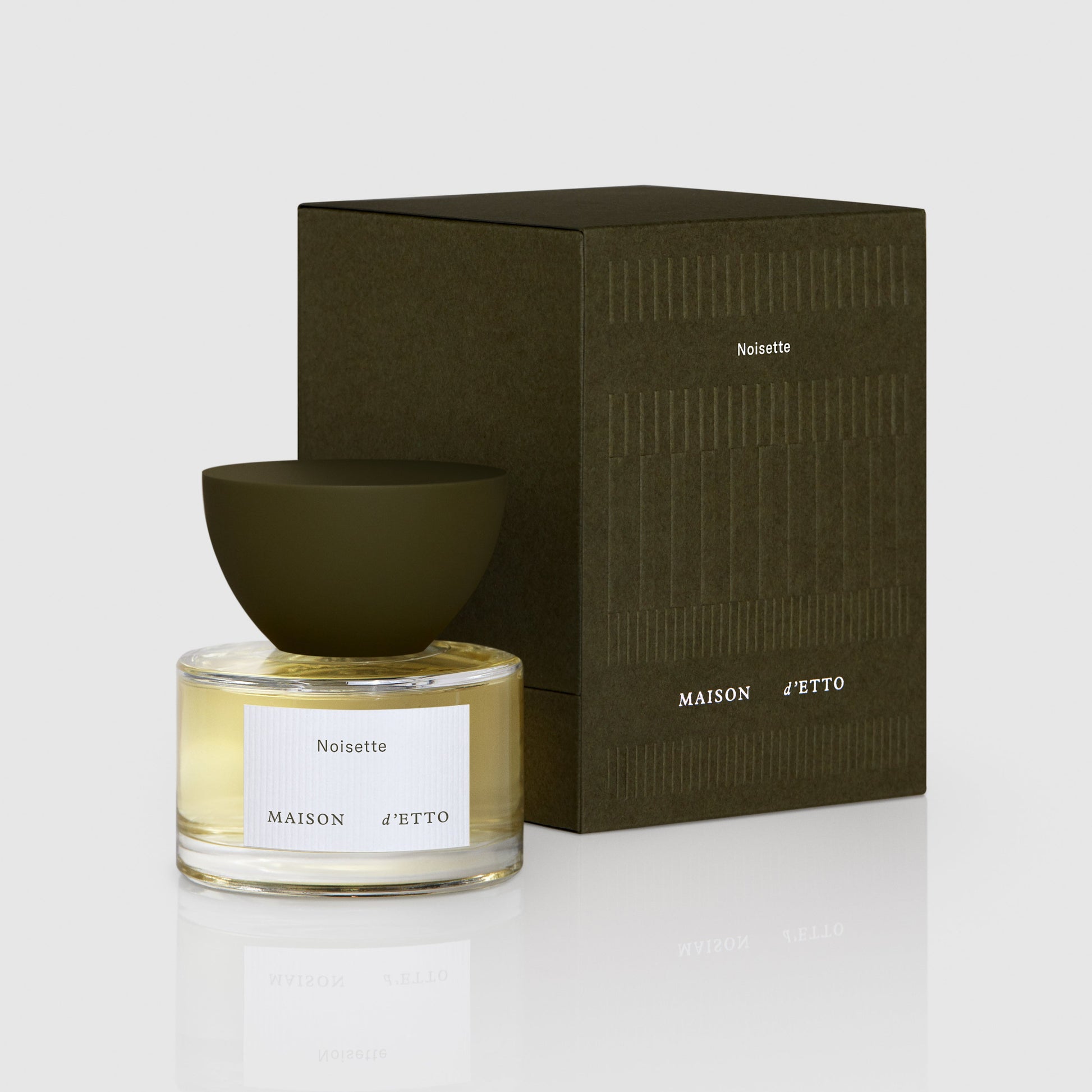 A clear glass bottle of maison d etto noisette fragrance with golden yellow liquid and a matte olive green bowl cap
