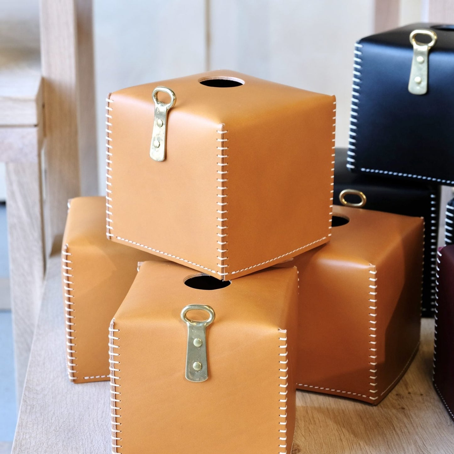 Tan leather tissue box cover with white stitching and brass colored metal clasp for stylish home use