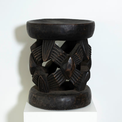 Black stone stool with intricate carvings on a white background