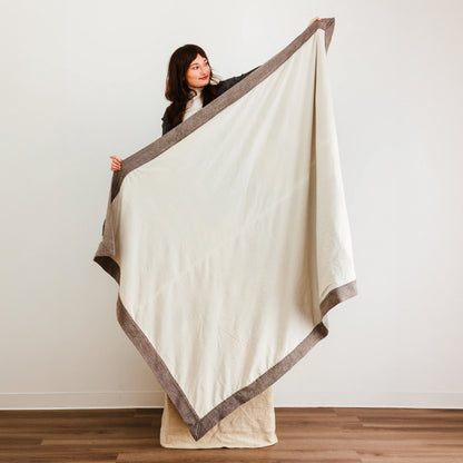 Large cream-colored quilt or blanket with a contrasting brown border.