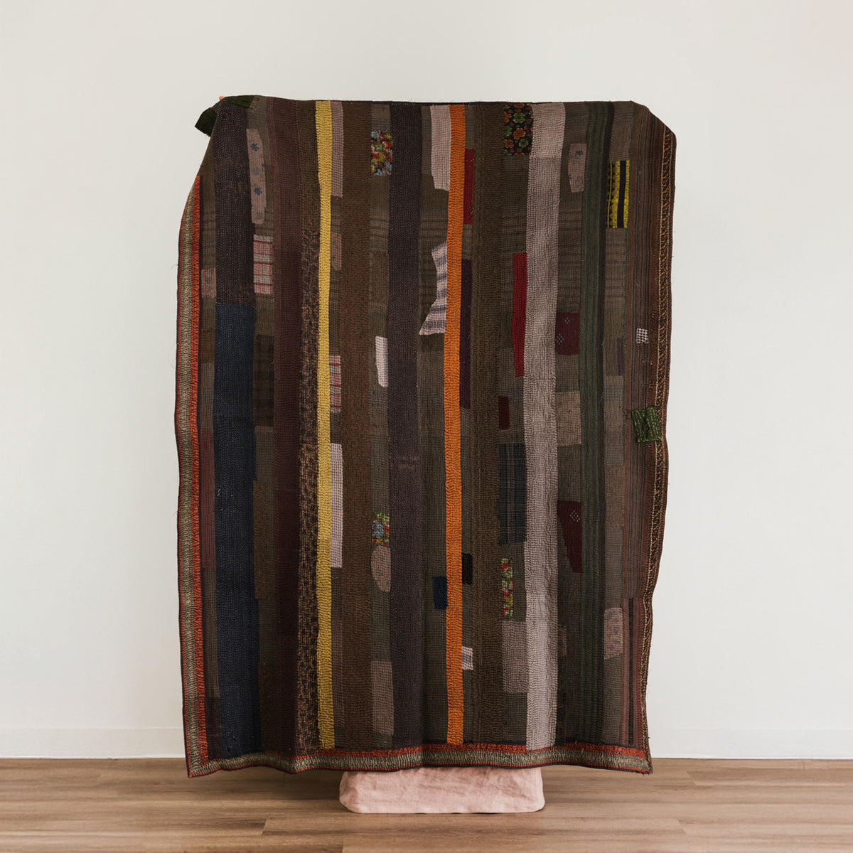 A rectangular patchwork throw blanket with vertical stripes in dark brown, black, beige, orange, and muted red.