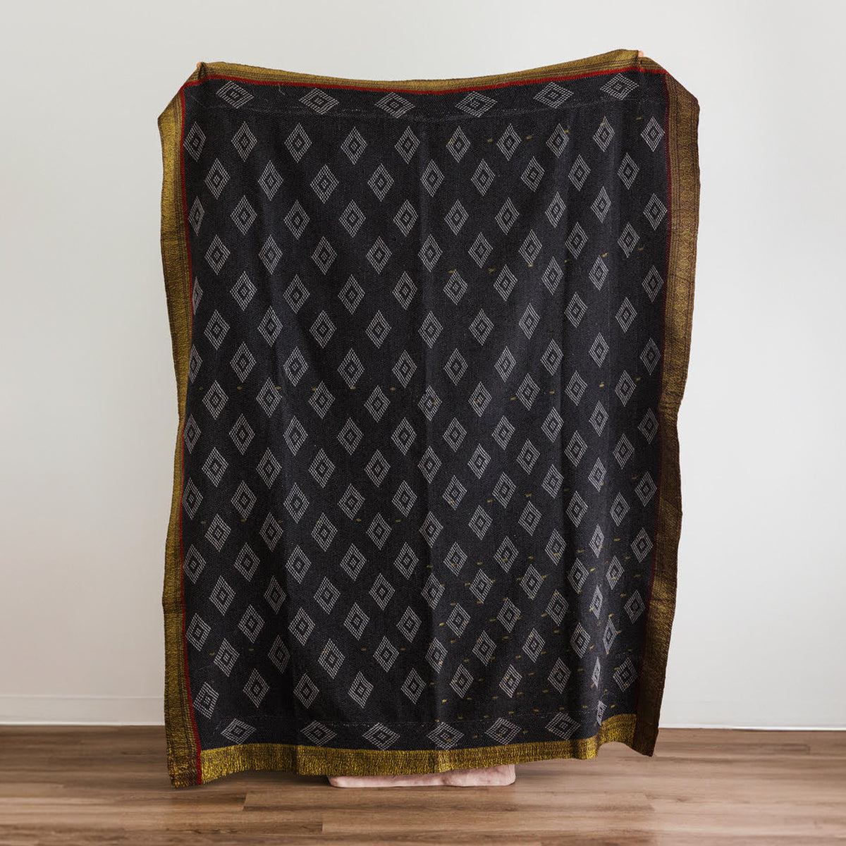 A black throw blanket with a repeating gray diamond pattern and a gold border.