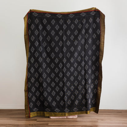 A black throw blanket with a repeating gray diamond pattern and a gold border.