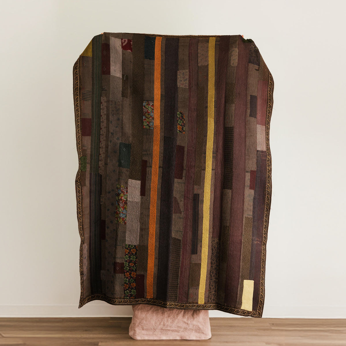 A patchwork quilted throw blanket with vertical stripes in earthy tones.