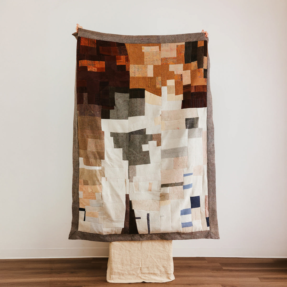 An abstract patchwork quilt with geometric blocks of brown, beige, white, gray, and muted blue.