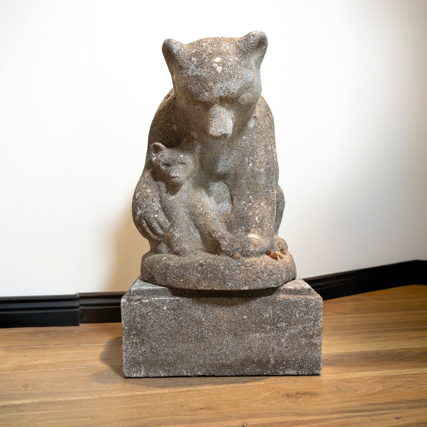 Stone sculpture of a bear with cubs on a wooden floor.