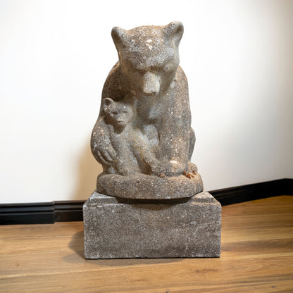 Stone sculpture of a bear with cubs on a wooden floor.