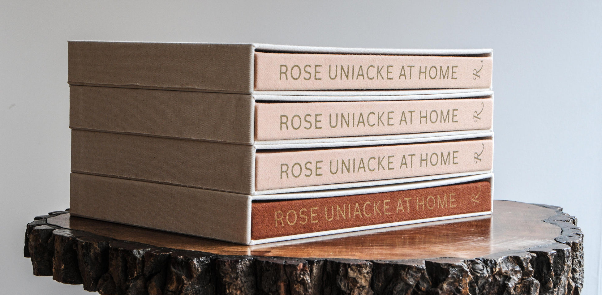 Stack of four hardcover books rose uniacke at home with beige spines and gold lettering on rustic wooden slice