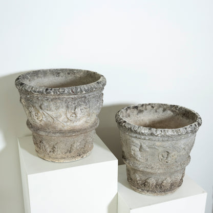 Two stone pots on white stands against a white background