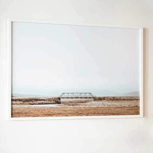 Framed photograph of a bridge over a field on a white wall