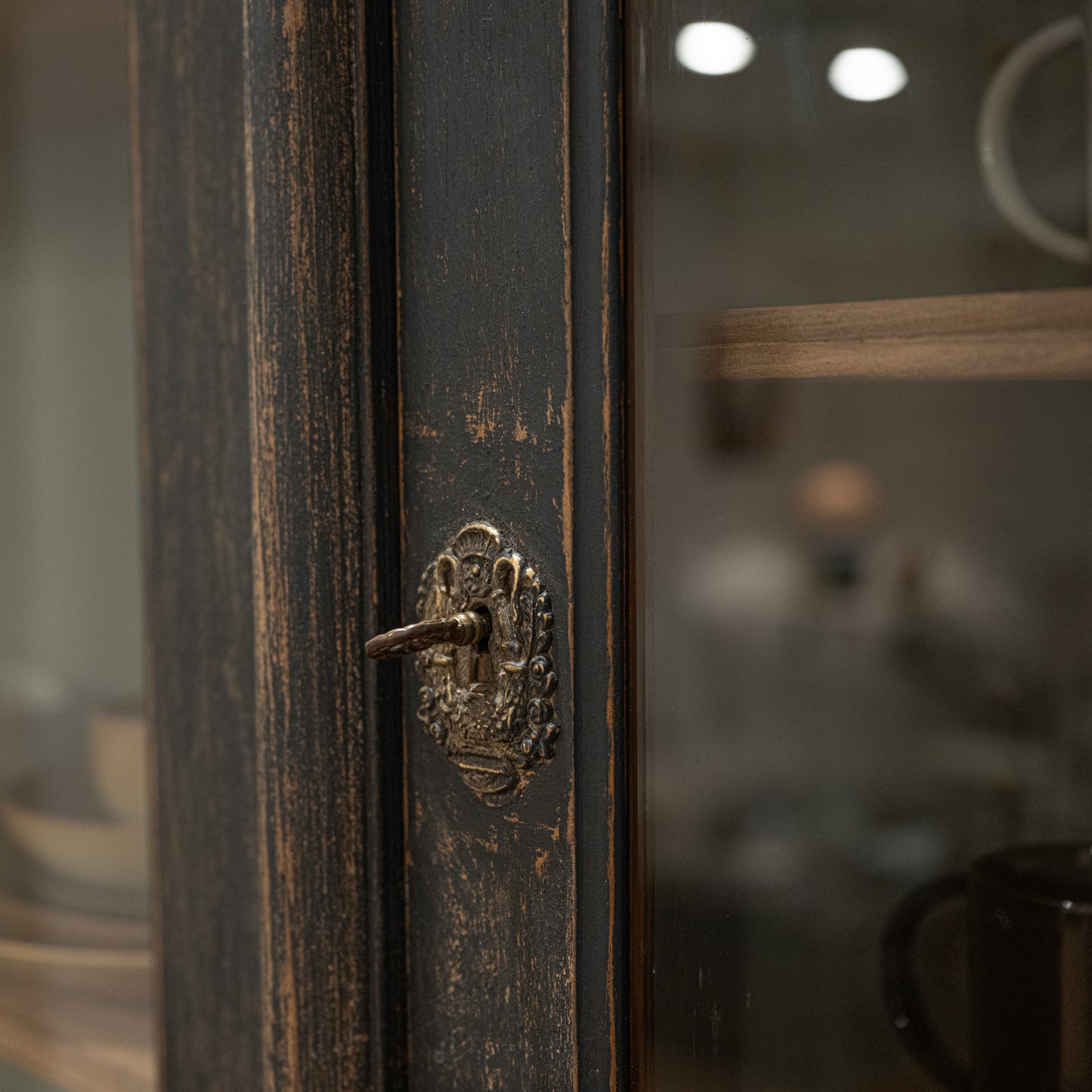 Antique-style brass door handle with ornate detail on dark distressed wood of late 19th century french display cabinet