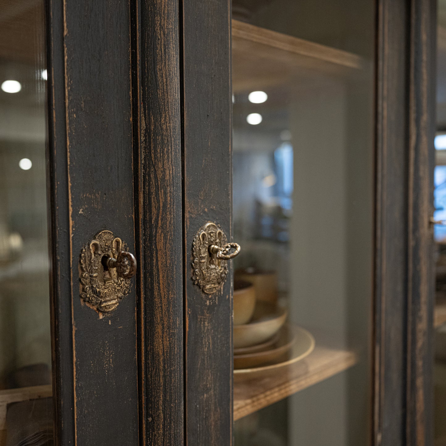 Antique-style brass door handles with ornate designs on dark-stained wooden cabinet doors of late 19th century french display cabinet